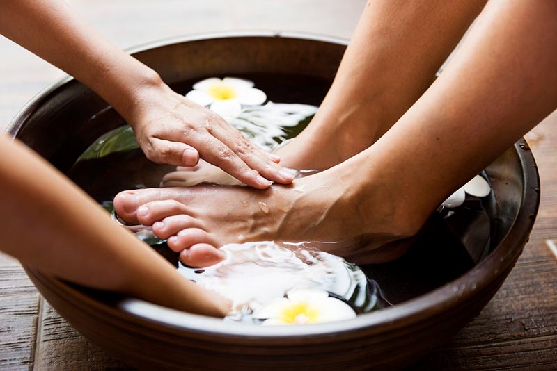 Hands giving feet a massage in bowl with water