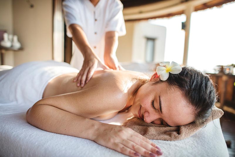 A happy lady lying on massage bed receiving a back massage