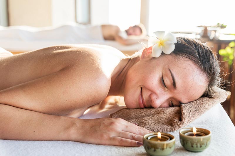 Relaxed lady lying on massage bed with candles waiting for massage to start